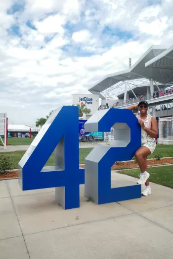 Woman posing inside a large blue “42” sculpture at JetBlue Park.